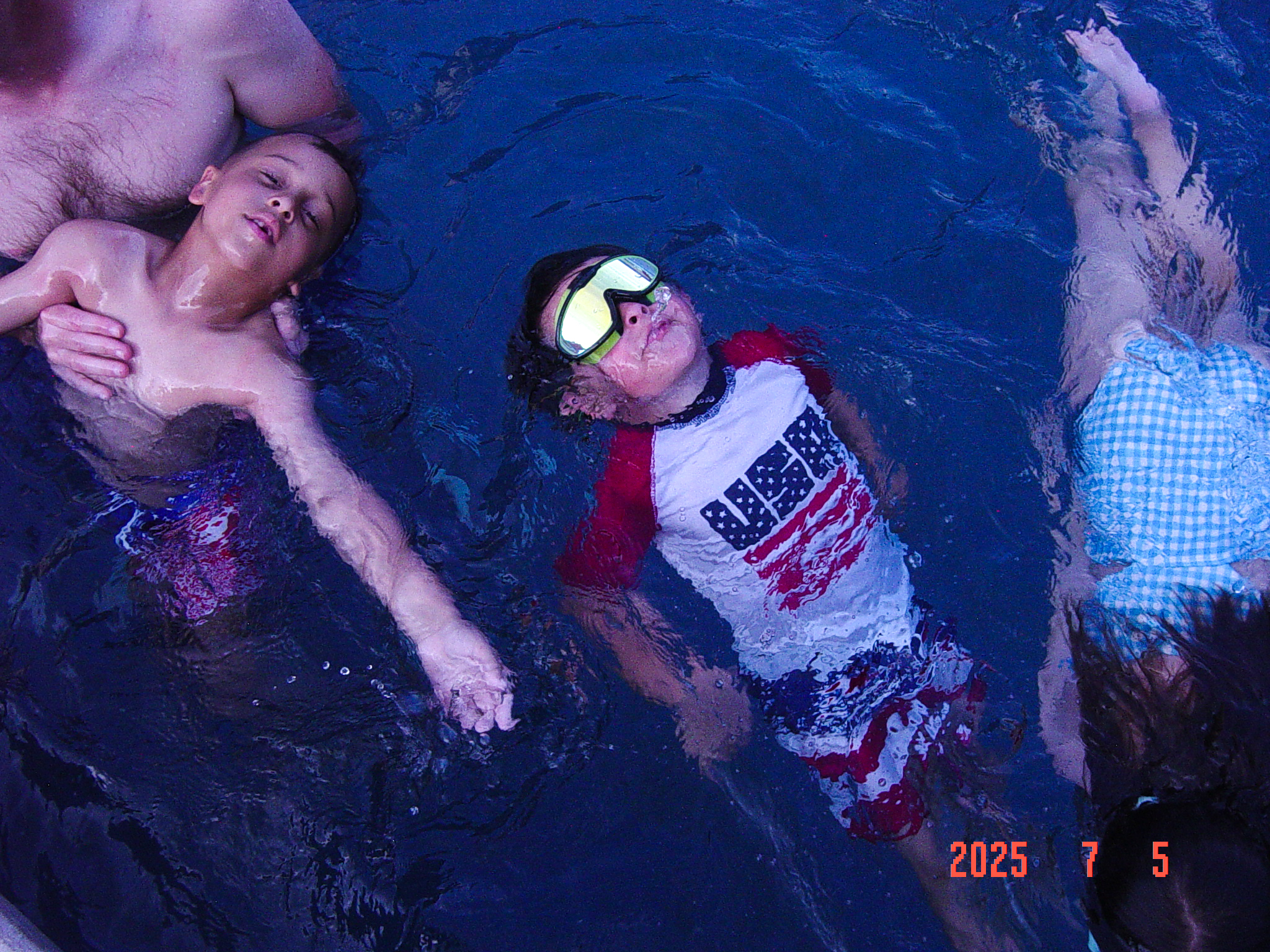 Kids floating on their backs in deep blue pool water, an orange in-camera date stamp in the corner