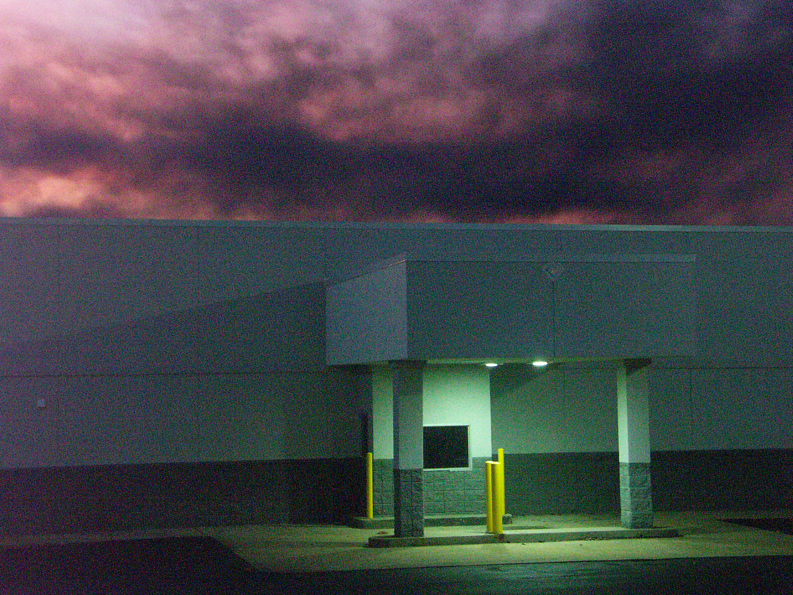 A big-box store at dusk under heavy pink and purple storm clouds, its lit entrance the one bright point
