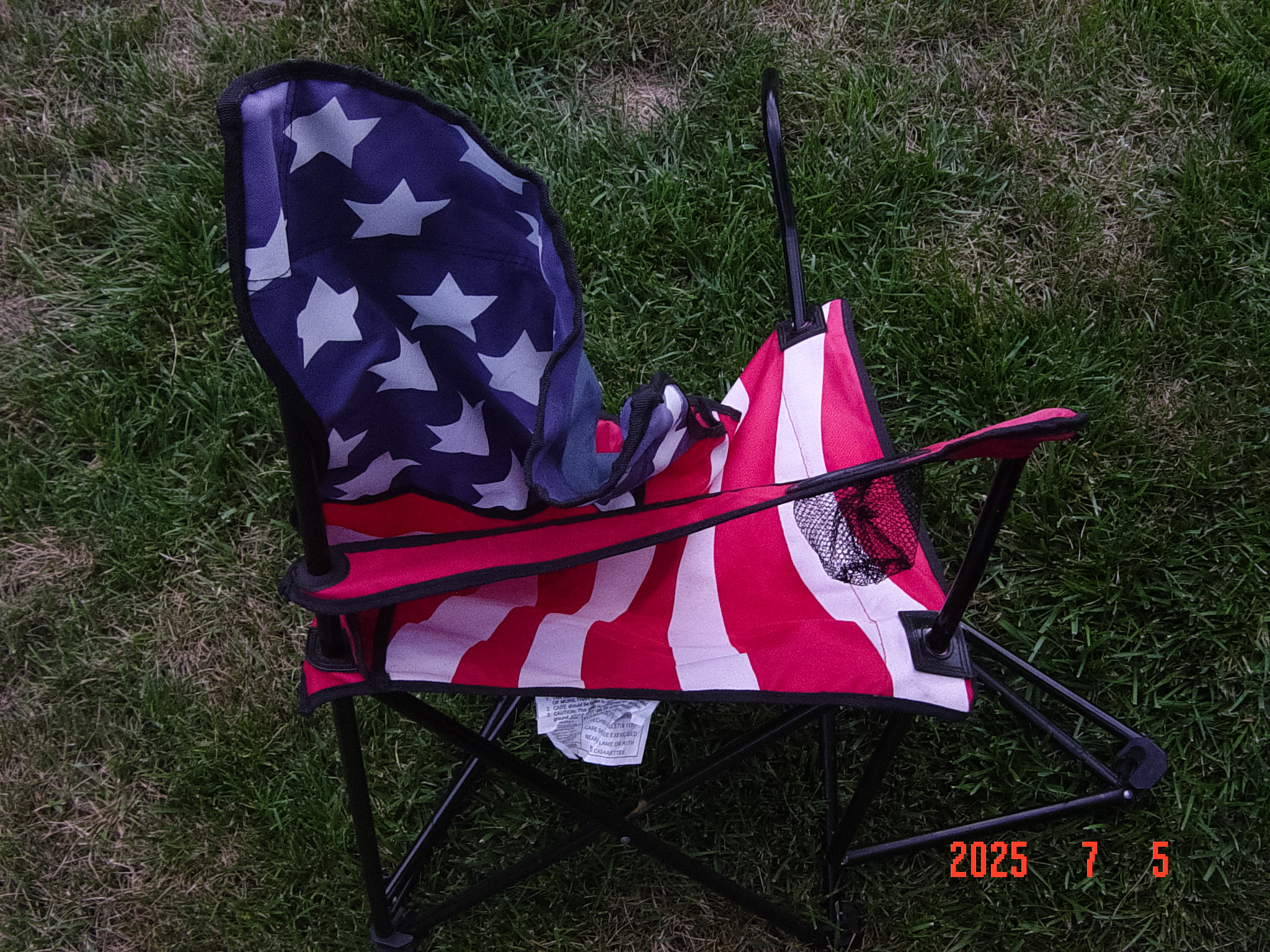 A folded American flag camp chair on grass, a small red in-camera date stamp glowing near the edge