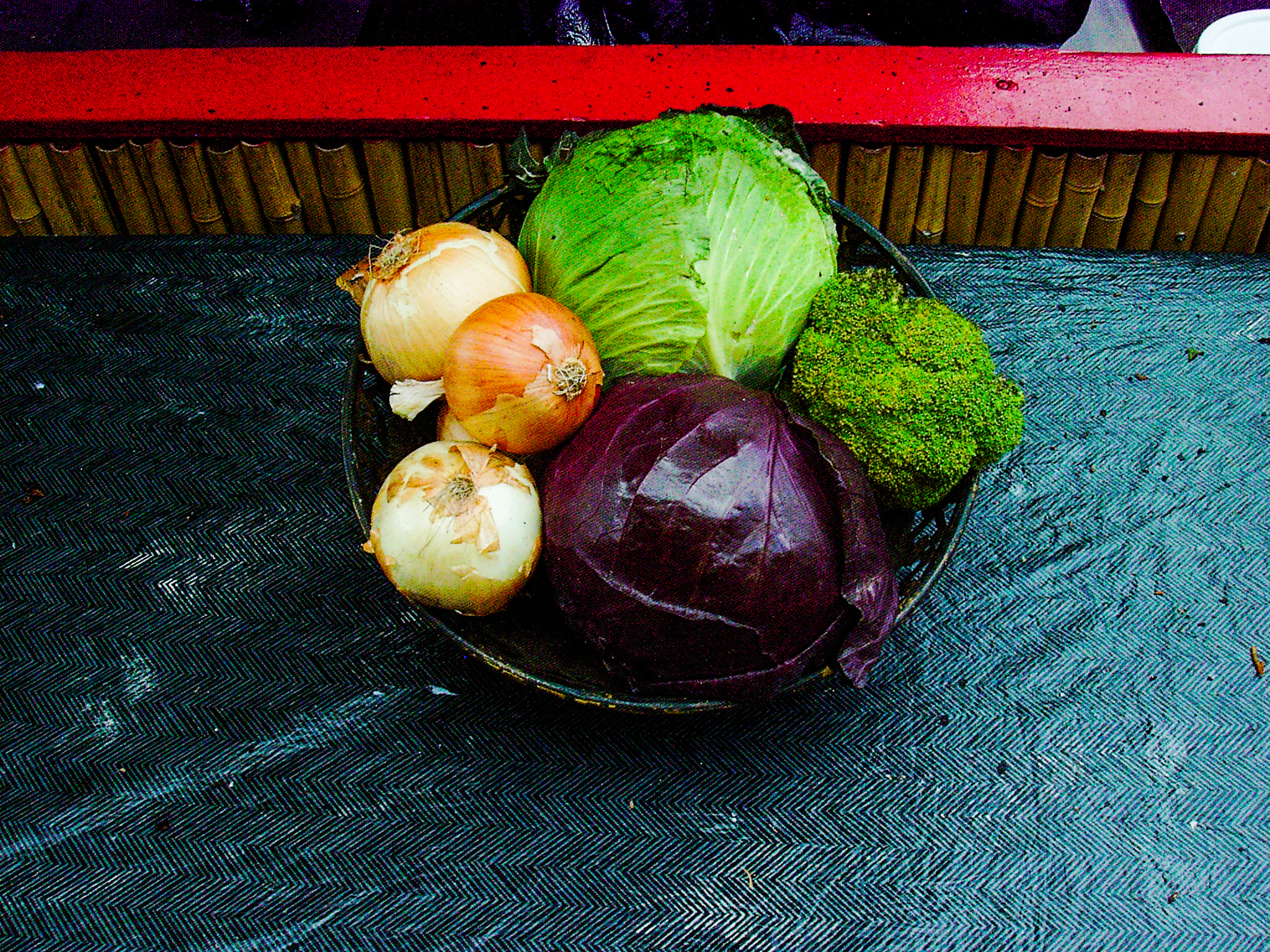 Onions, cabbage and eggplant gathered on a dark tabletop, flash color turning the vegetables glossy and unreal